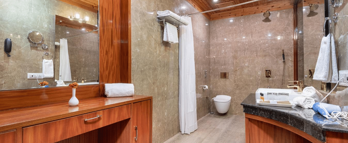 Image of a hotel bathroom with a wooden vanity, a mirror, and a shower  | DLS Serenity Resort and Spa